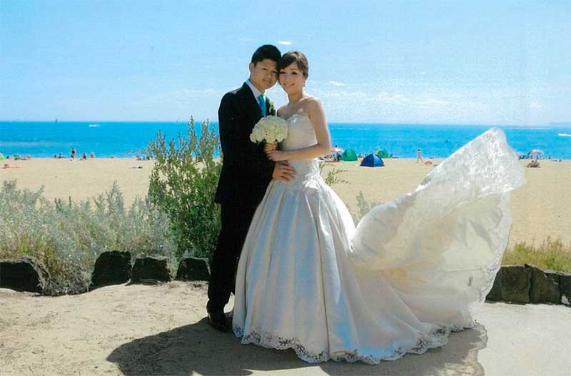 Photo of a bride and groom posing in front of Brighton Beach with the bride's dress flowing in the wind